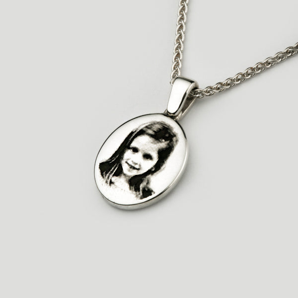 A silver oval signet necklace with a black and white photo engraving of a little girl.
